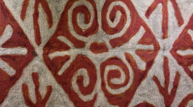 Traditional textile with red spiral and geometric Indigenous-inspired patterns.